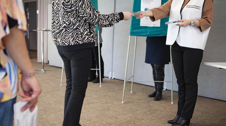 En person lämnar över ett röstkuvert till en röstmottagare i en vallokal.