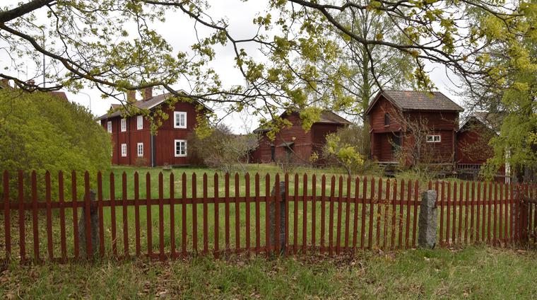 Gammel Jerkers från väster. Gården omgärdas av ett rött spjälstaket. Bostadshuset är en parstuga med mäktig panel. 
