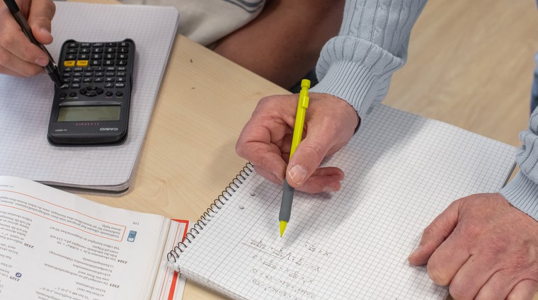 Miniräknare samt en hand som håller i en penna.