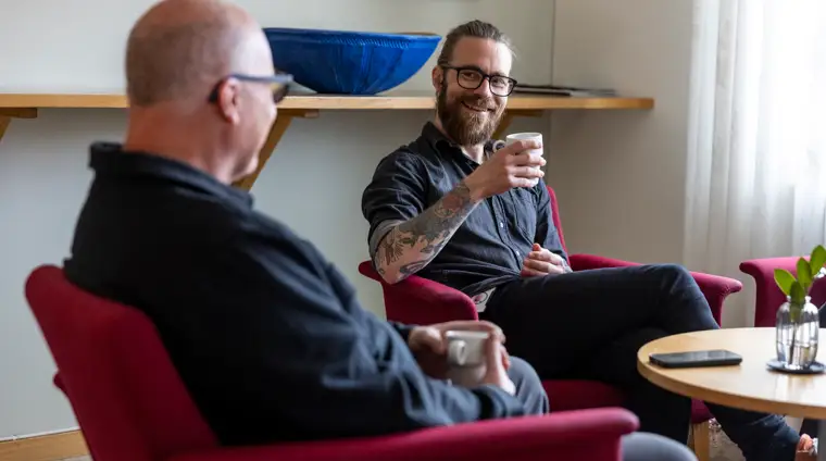 Två personer sitter ner i varsin fotölj och dricker kaffe.