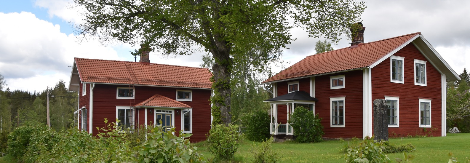 En gård med två faluröda hus med vita knutar.